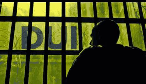 Silhouetted figure behind prison bars looking out at natural green light, symbolizing incarceration and criminal justice.
