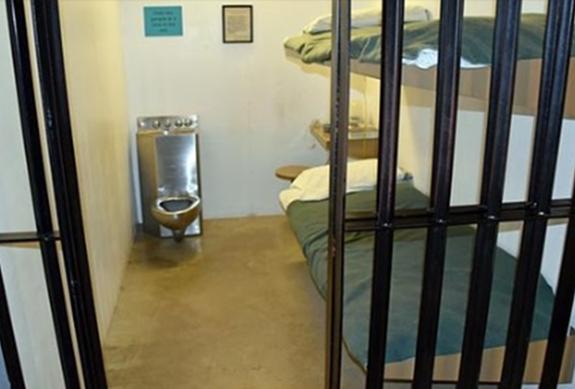 Prison cell interior with bunk bed, bars, and basic furnishings demonstrating incarceration conditions.
